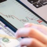 Smartfon z danymi giełdowymi leżący na banknocie dolara na biurku