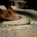 Mężczyzna zagniata ciasto na pizzę na oprószonym mąką blacie