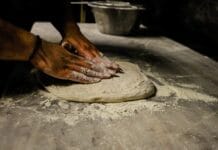 Mężczyzna zagniata ciasto na pizzę na oprószonym mąką blacie