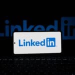Smartfon z logo LinkedIn na tle klawiatury i dużego logotypu w tle