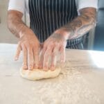 Tatuażysta kucharz zagniata ciasto na pizzę na oprószonym mąką blacie